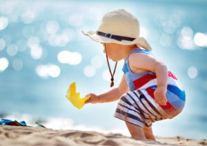 one year old boy playing at the beach in straw hat. Child with a paper ship at sea
